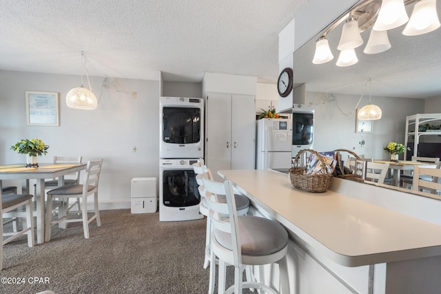 kitchen with a textured ceiling, a breakfast bar, stacked washer / dryer, freestanding refrigerator, and pendant lighting