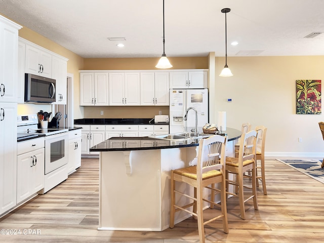 kitchen featuring a kitchen island with sink, light wood-type flooring, white appliances, and white cabinets