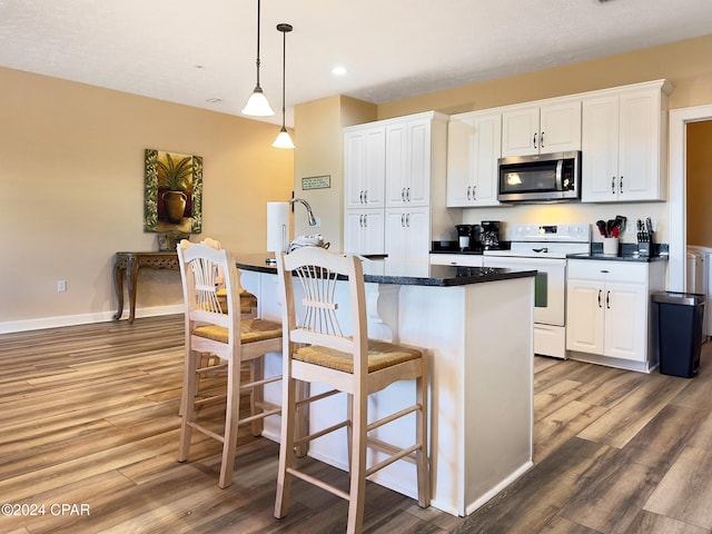 kitchen featuring electric range, pendant lighting, white cabinets, hardwood / wood-style flooring, and a center island with sink