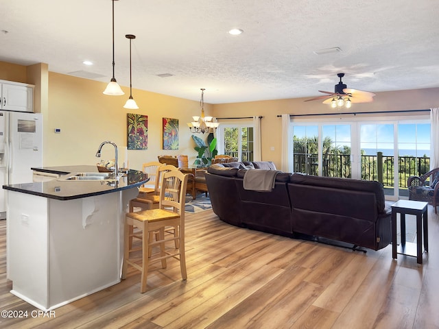 kitchen with white cabinets, ceiling fan with notable chandelier, pendant lighting, light hardwood / wood-style floors, and sink