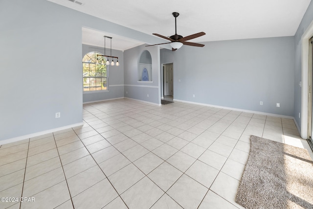 tiled empty room featuring vaulted ceiling and ceiling fan with notable chandelier