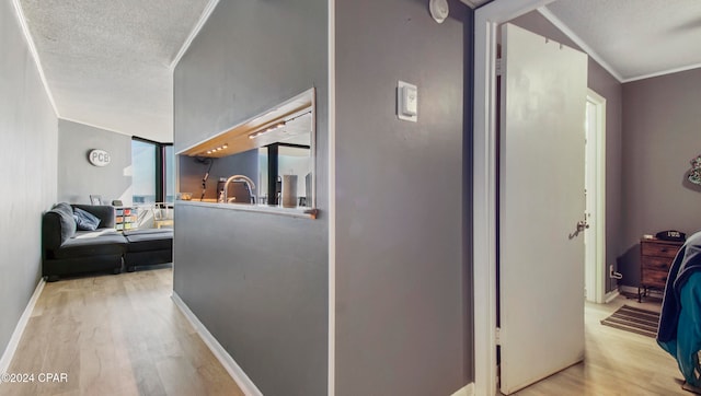 corridor with a textured ceiling, ornamental molding, and light wood-type flooring