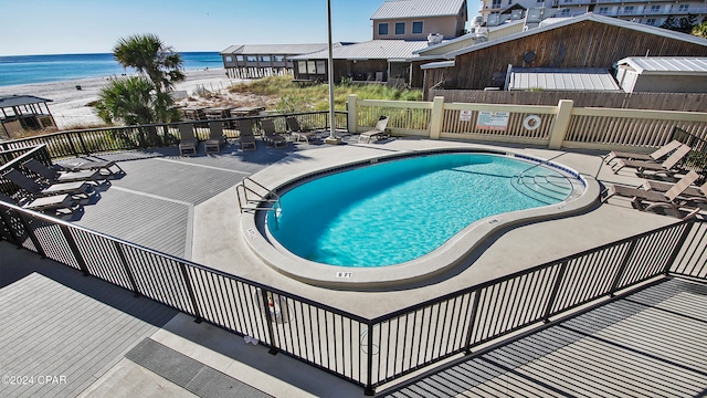 view of swimming pool featuring a water view, a patio, and a beach view