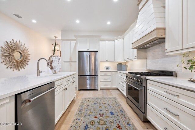 kitchen with premium range hood, white cabinets, hanging light fixtures, light wood-type flooring, and stainless steel range