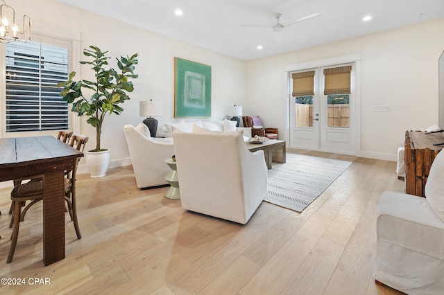 living area with ceiling fan with notable chandelier, plenty of natural light, light wood-style flooring, and baseboards