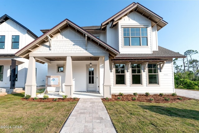 view of front of home featuring covered porch, roof with shingles, and a front lawn