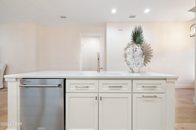 kitchen featuring a sink, white cabinetry, light wood-style floors, stainless steel dishwasher, and an island with sink