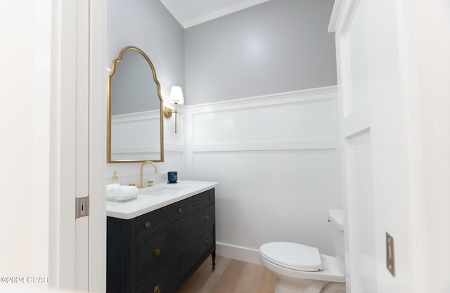 half bath with toilet, a wainscoted wall, wood finished floors, vanity, and a decorative wall