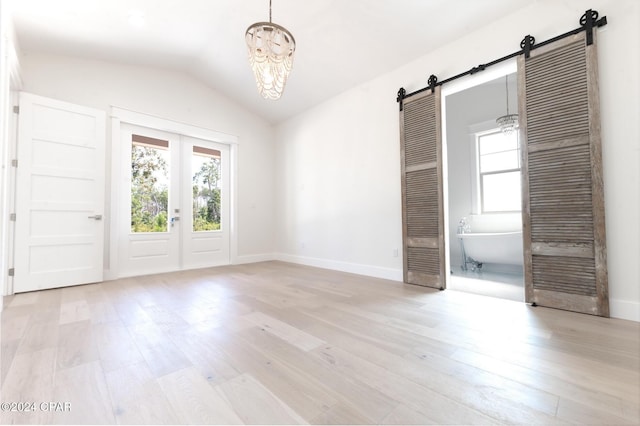 unfurnished room featuring vaulted ceiling, a barn door, light wood-style flooring, and a healthy amount of sunlight