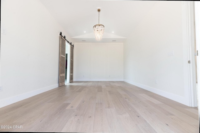 empty room with lofted ceiling, a chandelier, a barn door, light wood-style flooring, and baseboards