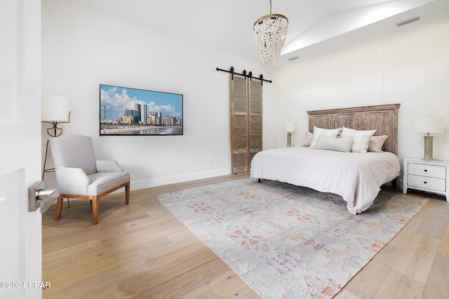 bedroom featuring a barn door, light wood-type flooring, visible vents, and a notable chandelier