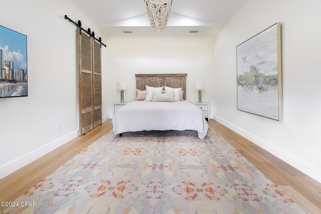 unfurnished room with french doors, vaulted ceiling, a barn door, a notable chandelier, and light hardwood / wood-style floors