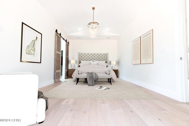 unfurnished room featuring a notable chandelier, lofted ceiling, a barn door, and light hardwood / wood-style floors