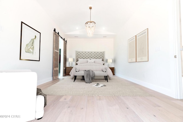 bedroom featuring light wood-type flooring, a barn door, baseboards, and lofted ceiling