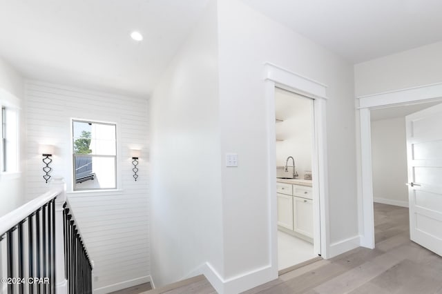 corridor featuring light wood-type flooring, baseboards, a sink, and recessed lighting