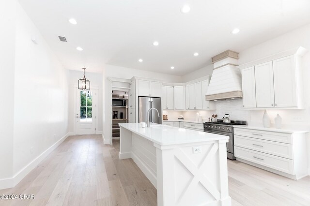 kitchen featuring custom exhaust hood, white cabinets, hanging light fixtures, light hardwood / wood-style flooring, and premium appliances