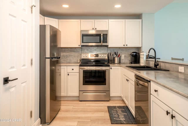 kitchen featuring appliances with stainless steel finishes, sink, backsplash, white cabinetry, and light hardwood / wood-style flooring