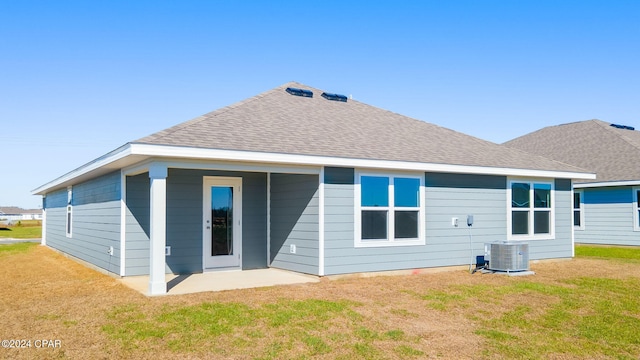 rear view of property with central air condition unit, a shingled roof, and a yard