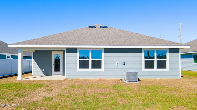 rear view of property featuring a patio, a shingled roof, a lawn, central AC unit, and fence