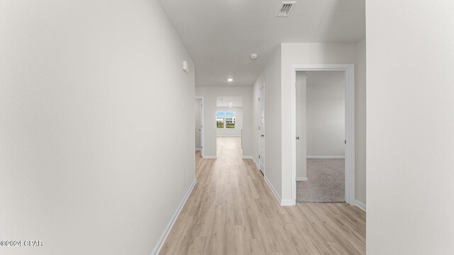 corridor featuring light wood finished floors, baseboards, and visible vents