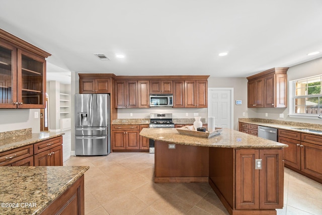 kitchen featuring a kitchen island, light stone countertops, stainless steel appliances, and light tile patterned flooring