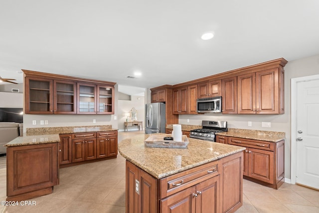 kitchen featuring light tile patterned flooring, stainless steel appliances, light stone counters, and a kitchen island