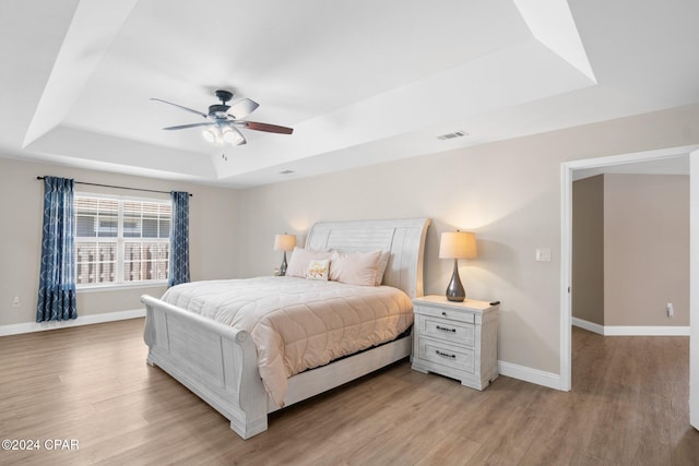 bedroom featuring light hardwood / wood-style floors, a tray ceiling, and ceiling fan