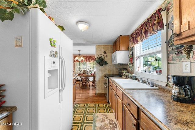 kitchen with pendant lighting, white appliances, sink, and a notable chandelier