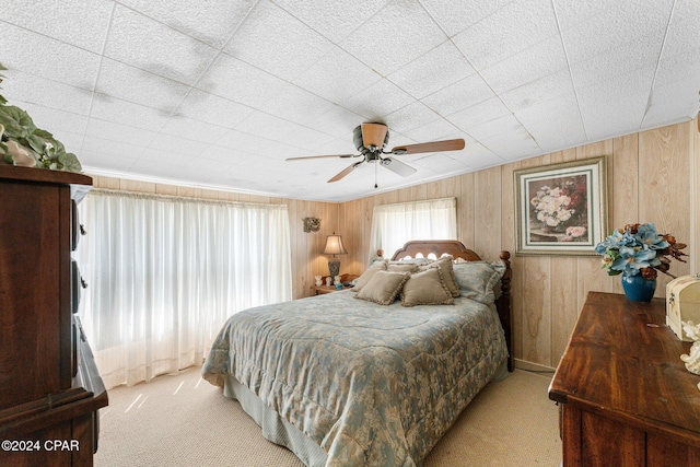 carpeted bedroom with ceiling fan and wood walls