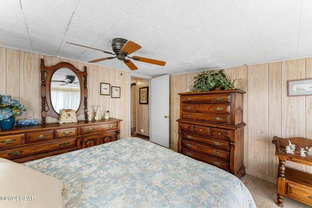 carpeted bedroom featuring ceiling fan and wooden walls