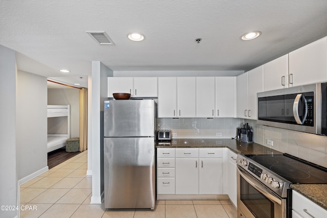 kitchen with tasteful backsplash, stainless steel appliances, dark stone counters, white cabinetry, and light tile patterned floors