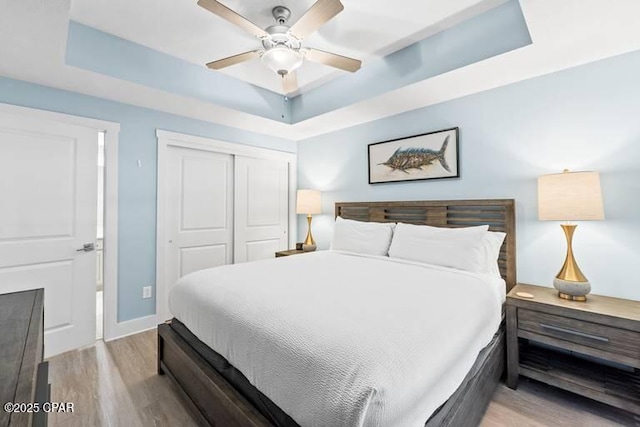 bedroom featuring a raised ceiling, ceiling fan, light hardwood / wood-style floors, and a closet