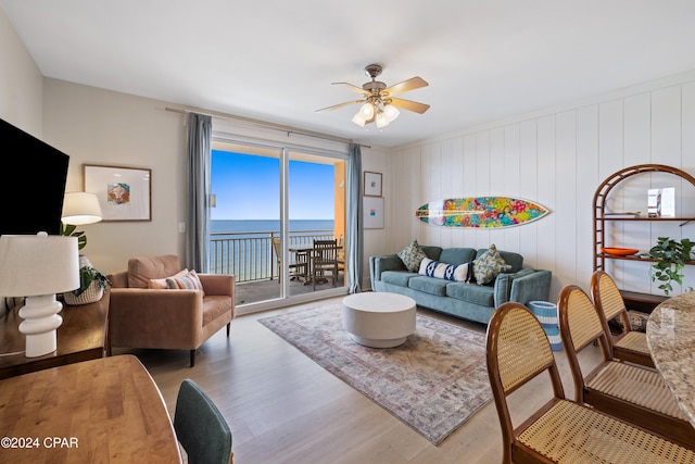 living room with a water view, ceiling fan, wooden walls, and wood-type flooring