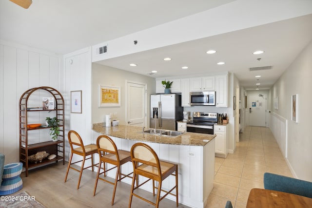 kitchen with stainless steel appliances, white cabinets, kitchen peninsula, a breakfast bar, and stone countertops