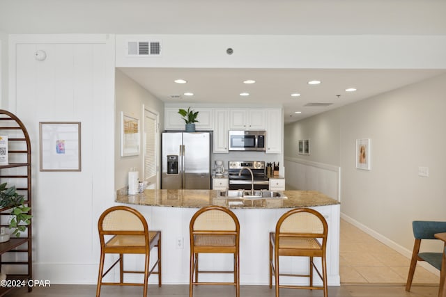 kitchen with stainless steel appliances, a kitchen bar, white cabinets, dark stone countertops, and kitchen peninsula