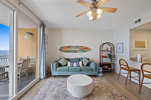 living room featuring ceiling fan, wood-type flooring, wood walls, and a water view