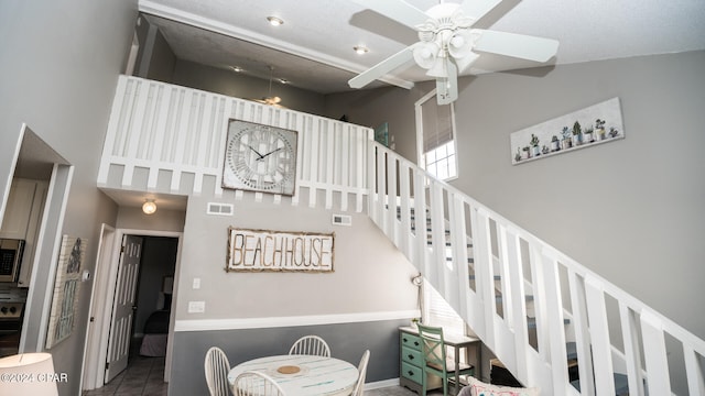 stairs featuring ceiling fan, a textured ceiling, a high ceiling, and tile patterned flooring