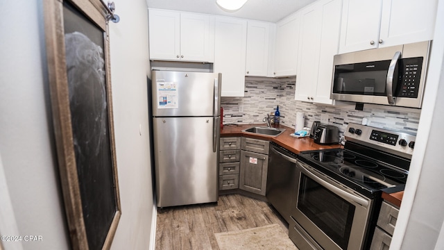 kitchen with white cabinets, butcher block counters, sink, light hardwood / wood-style floors, and stainless steel appliances