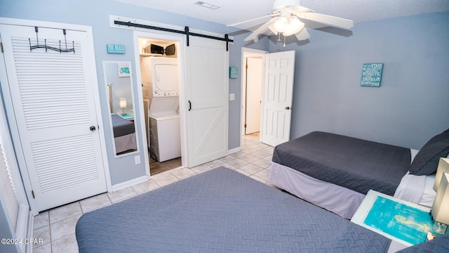 bedroom featuring a barn door, a textured ceiling, ceiling fan, stacked washer and dryer, and light tile patterned floors