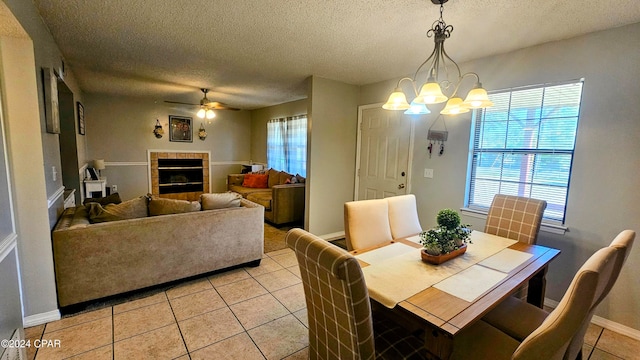 dining area featuring a textured ceiling, a tiled fireplace, ceiling fan with notable chandelier, and light tile patterned floors