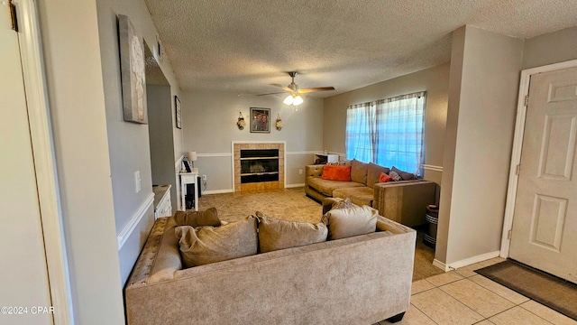 living room featuring a textured ceiling, light tile patterned flooring, a fireplace, and ceiling fan