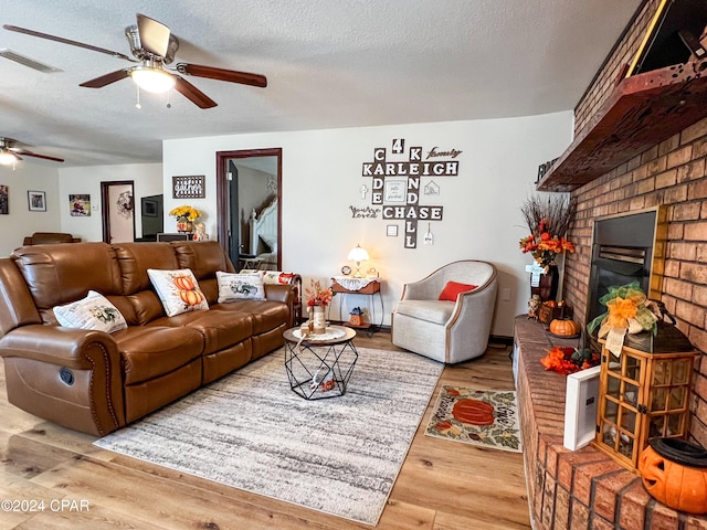 living room with hardwood / wood-style floors, ceiling fan, a textured ceiling, and a brick fireplace