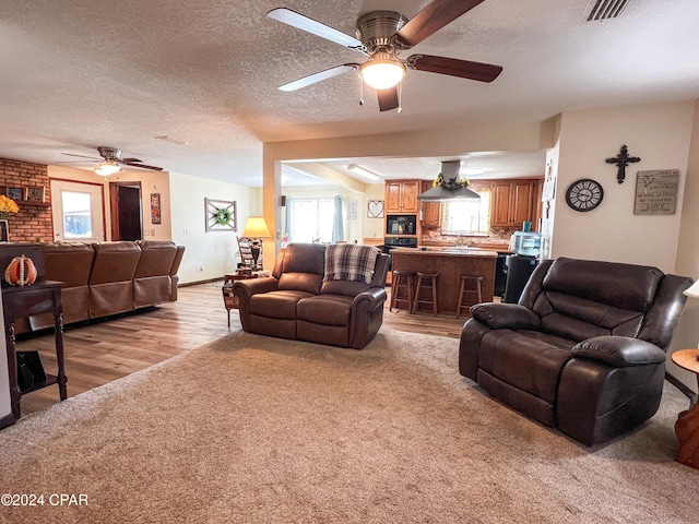 living room with ceiling fan, a textured ceiling, and light hardwood / wood-style flooring