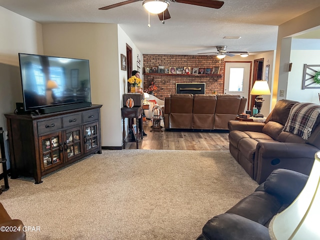 living room with hardwood / wood-style floors, a textured ceiling, a brick fireplace, and ceiling fan