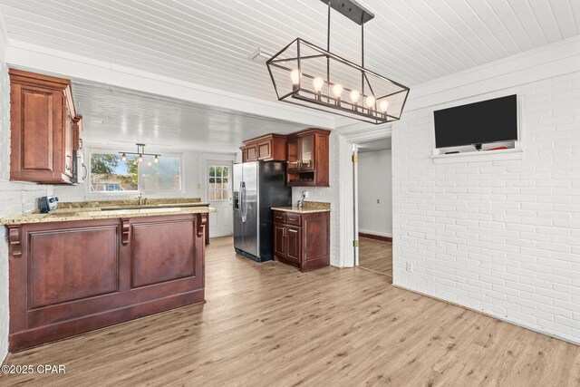 kitchen with stainless steel fridge, light hardwood / wood-style floors, brick wall, decorative light fixtures, and kitchen peninsula