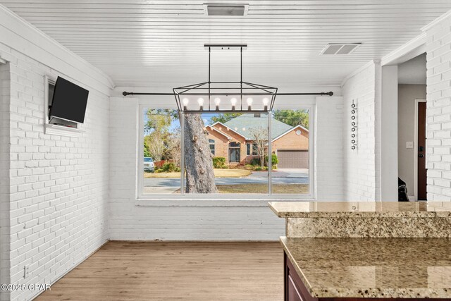 unfurnished dining area with an inviting chandelier, light wood-type flooring, and brick wall