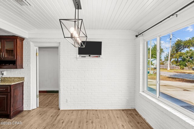 unfurnished dining area featuring lofted ceiling, wood ceiling, light hardwood / wood-style flooring, and brick wall