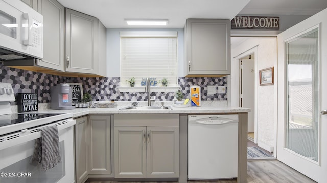 kitchen with sink, gray cabinetry, decorative backsplash, light hardwood / wood-style floors, and white appliances