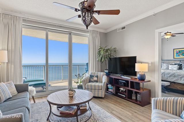 living room with ornamental molding, a water view, light wood-type flooring, a textured ceiling, and ceiling fan