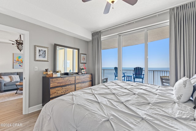 bedroom featuring access to outside, a textured ceiling, ceiling fan, a water view, and light hardwood / wood-style flooring